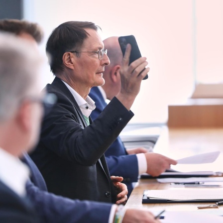 Karl Lauterbach hält bei einer Pressekonferenz sein Handy in die Höhe