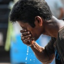 Ein indischer Mann spritzt sich mit der rechten Hand Wasser ins Gesicht.