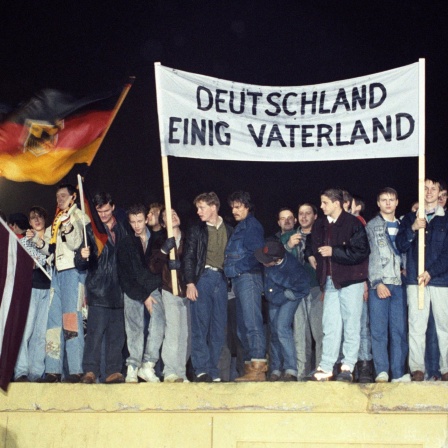 Mit der Deutschlandfahne und einem Transparent &#034;Deutschland Einig Vaterland&#034; stehen zahlreiche Berliner am 22.12.1989 auf der Berliner Mauer am Brandenburger Tor.