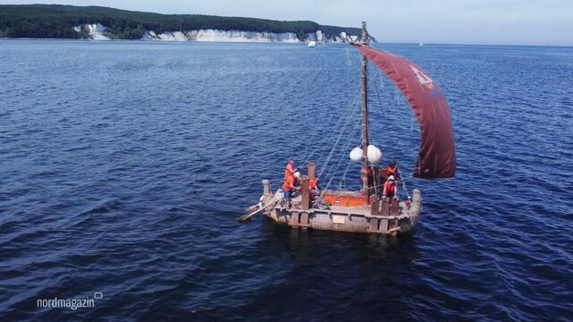 Eine Replik eines Schilfbootes mit geblähtem, dunkelroten Segel auf der Ostsee.