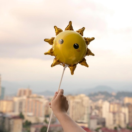 Eine Kinderhand hält einen Sonnenluftballon.