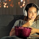 Eine Frau isst Popcorn, lächtelt und schaut auf ihrem Laptop einen Film mit Kopfhörern 