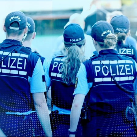 Von hinten zu sehende Polizist:innen, die in einer Menschenmenge unterwegs sind