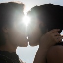 Zwei Frauen küssen sich, ein heller Sonnenstrahl leuchtet auf ihre Gesichter.