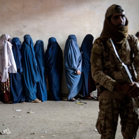 Ein Taliban-Kämpfer steht Wache, während Frauen darauf warten, von einer humanitären Hilfsorganisation verteilte Lebensmittelrationen zu erhalten.