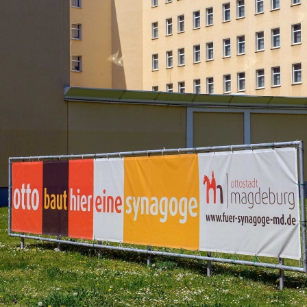 "Otto baut hier eine Synagoge" steht auf einem Banner das über eine Wiese gespannt ist.