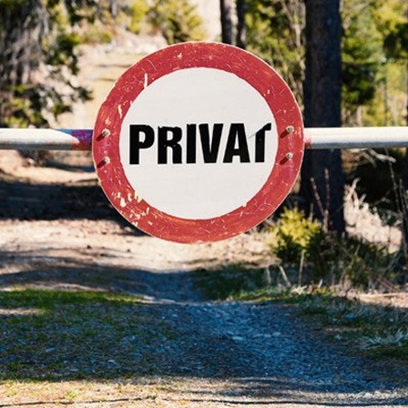 Ein Waldweg, der mit einer Schranke versperrt ist. An der Schranke ist ein Schild mit der Aufschrift "Privat" angebracht.