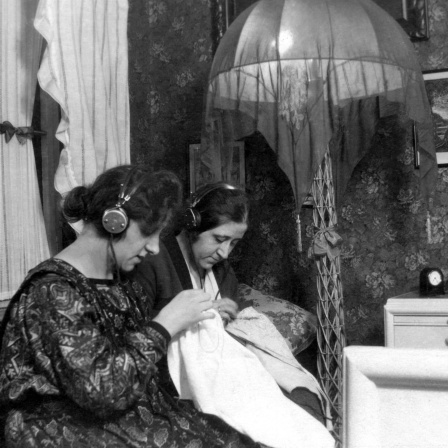 Zwei Frauen hören in den 1930ern mit Kopfhörer Radio und sticken: 1923 begann der reguläre Rundfunkbetrieb in Deutschland - maßgeblich vorangetrieben vom weitgereisten Ingenieur und Ministerialdirektor Hans Bredow