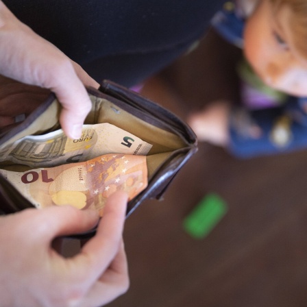 Blick in eine geöffnete Geldbörse mit nur 15 Euro, im Hintergrund ein kleines Kind