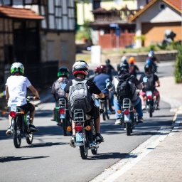 Minschen mit Simson Mopeds fahren durch eine Ortschaft.