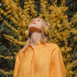 Das Beitragsbild des WDR3 Kulturfeature "Durch die Blume hören" zeigt eine Frau mit Kopfhörern vor einem gelb blühendem Baum