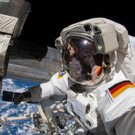 Ein Astronaut mit deutschem Hoheitsabzeichen auf seinem Raumanzug arbeitet außerhalb der ISS im Weltraum. 