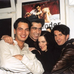 Yüksel Yavuz und drei Darsteller*innen des Filmes "Aprilkinder" liegen sich lachend in den Armen. Im Hintergrund ist das Filmplakat zu sehen.