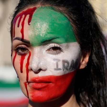 Eine Teilnehmerin einer Solidaritätsdemonstration in Italien mit den Protestierenden im Iran ist mit einer Iranischen Flagge und rotem Blut geschminkt. 