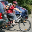 Ein Junge fährt mit seinem Fahrrad auf dem Weg zur Schule zwischen geparkten Autos auf die Straße.