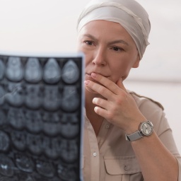 Eine Frau mit einem Kopftuch schaut nachdenklich auf eine Computertomographie eines Schädels.