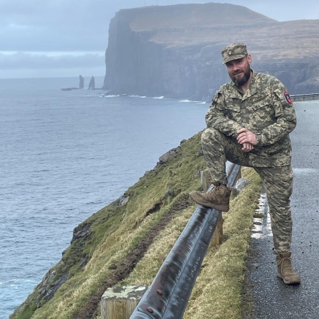 Bjørn Kallsoys steht an einer Klippe in seiner Uniform im rechten Bildrand und lächelt in die Kamera.