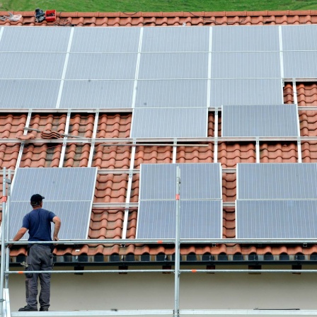 Symbolbild: Ein Arbeiter installiert auf einem Dach eine Solaranlage