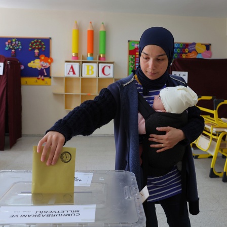 Eine Frau mit einem Baby auf dem Arm wirft ihren Stimmzettel in einem Wahllokal in Ankara in eine Wahlurne. 