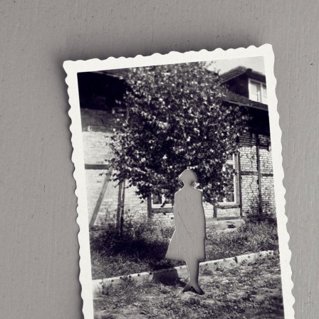 Auf einer grauen Fläche liegt eine alte schwarz weiss Fotografie, mit einer aus dem Foto herausgeschnittenen Person.