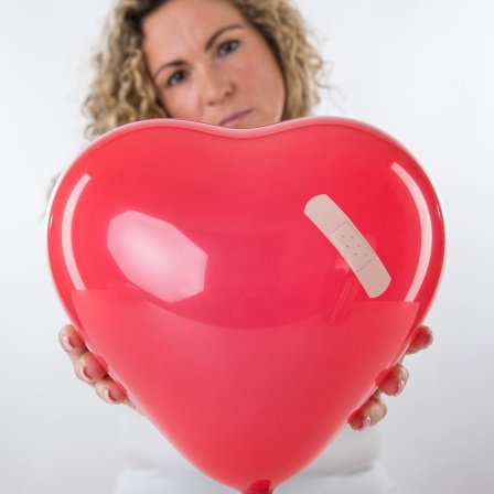 Eine Frau hält einen Luftballon in Herzform, der mit einem Pflaster beklebt ist.
