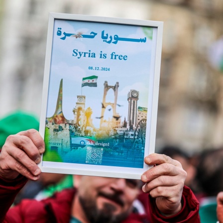 Ein Mann mit einem Schild mit dem Schriftzug "Syria is free" und dem Datum des 08.12.2024 auf einer Demonstration in Wuppertal