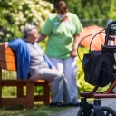 Ein Rollator steht nahe einer Pflegefachkraft und einer Bewohnerin eines Seniorenheims.