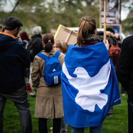 Eine Teilnehmerin eines Ostermarsches hat sich in eine Flagge mit einer Friedenstaube gewickelt.