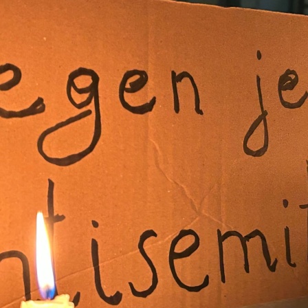 Eine brennende Kerze steht vor einem Schild mit der Aufschrift &#034;Gegen jeden Antisemitismus&#034;