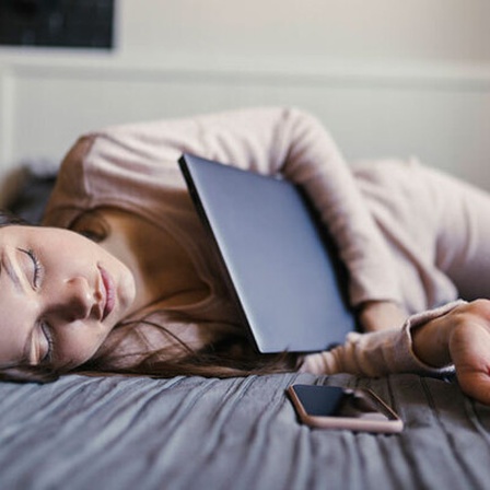 Eine Frau ist mit ihrem Laptop im Arm auf ihrem Bett eingeschlafen.