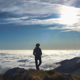 Eine Person steht in den Bergen einsam über einem Meer von Wolken