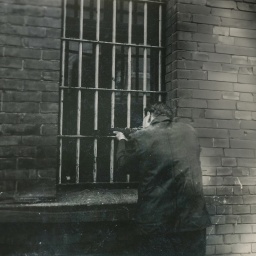 Mann hält Waffe aus einem vergitterten Fenster