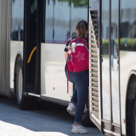 Eine Schülerin steigt an einer Bushaltestelle in einen Bus