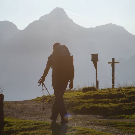 Wanderer mit Rucksack und Trekkingstöcken im Gegenlicht vor Bergkulisse unterwegs zur Gotzenalm, Schönau am Königssee, Berchtesgadener Land