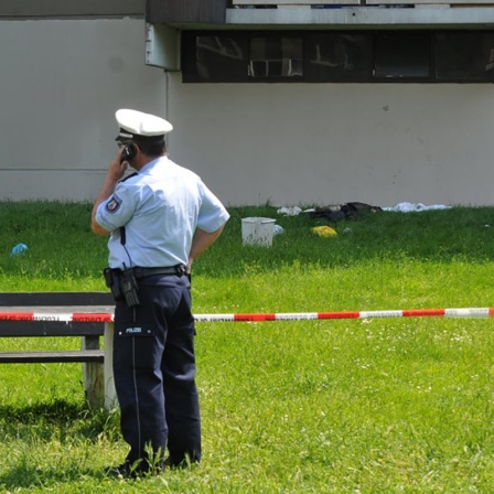 Ein telefonierender Polizist steht vor einer Absperrung vor einer Schule (Archivbild)