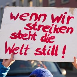 Eine Demonstrantin hält ein Schild hoch mit der Aufschrift: " Schild: Wenn wir Streiken steht die Welt still"