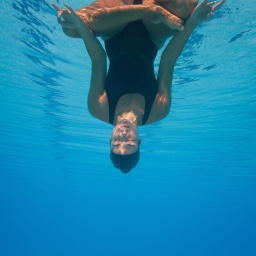 Eine Frau kopfüber unter Wasser in Meditationshaltung.