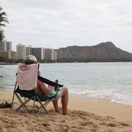 Ein Mann sitzt auf einem Stuhl am Strand. (Quelle: Picture Alliance)