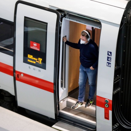 Ein Fahrgast mit FFP2 Maske steht im Eingang eines ICE Zuges und schaut heraus. 