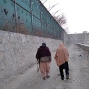 Zwei Männer laufen an einer hohen Mauer mit Stacheldraht, einer trägt ein Gewehr unter dem Arm, Afghanistan 2022.