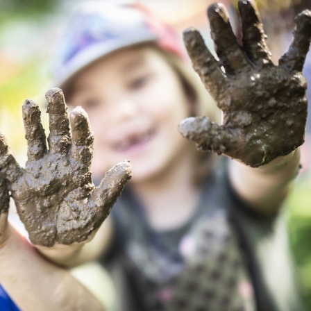 Zwei Kinder zeigen ihre Matschhände im Garten der "Freien Kinderschule" im Stadtteil Unterliederbach. Die Einrichtung existiert seit über 40 Jahren. Angefangen hat alles 1969 in Schwalbach, als Eltern einen der ersten Kinderläden gründeten.