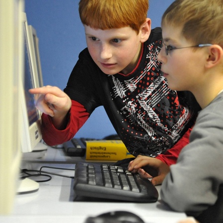 Etwa zwölf Jahre alte Kinder sitzen vor Computern.