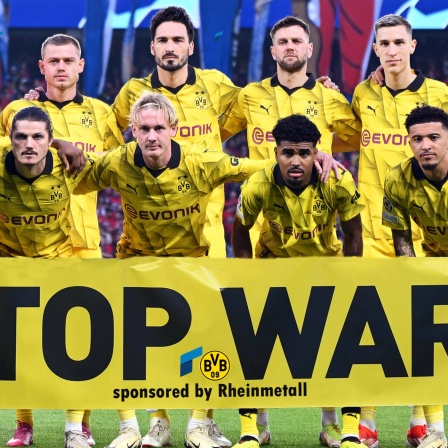 Die Mannschaft von Borussia Dortmund hält ein Banner, darauf steht: Stop War - sponsored by Rheinmetall