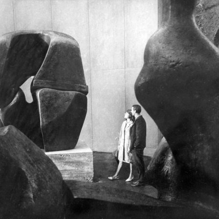 Historisches Schwarzweißfoto eines jungen Paares, das Steinskulpturen in einer Halle betrachtet.
