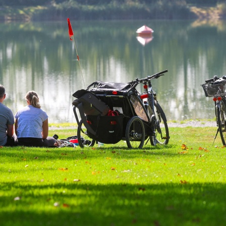 Ein Mann und eine Frau sitzen neben ihren Fahrrädern an einem See in der Sonne
