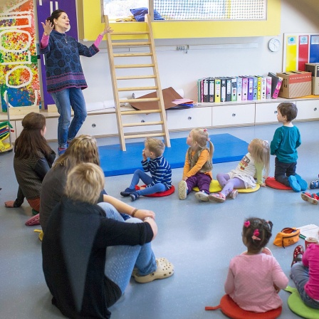 In einer bilingualen Kita in Schwerin agiert eine Erzieherin mit Kindern in einem Sitzkreis.