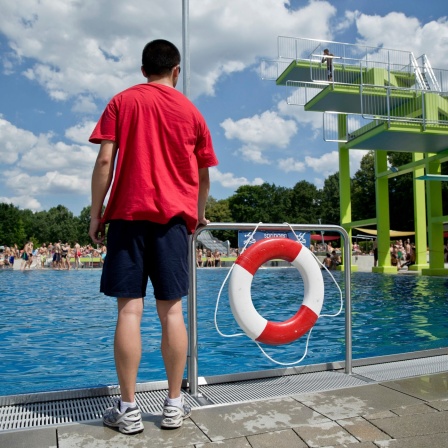 Ein Bademeister steht neben einem Rettungsreifen vor einem Schwimmbecken