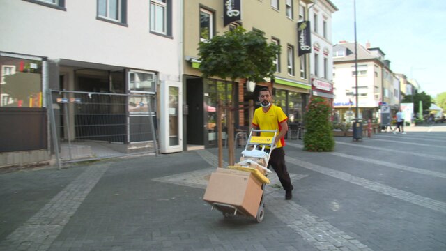 Postbote transportiert Pakete mit Rollwagen