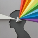Aus Papier geschnittene Illustration eines Kopfes in dessen Mitte ein Prisma sitzt welches einen grauen Lichtstrahl in das gesamte Spektrum bricht