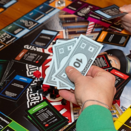 Spieler vertiefen sich in eine Monopoly-Runde mit farbigen Geldscheinen, Spielkarten und Würfeln.